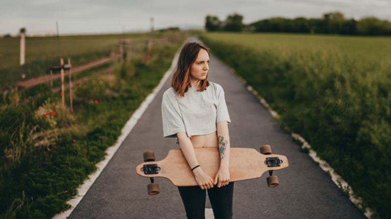 Tjej ståendes på en väg hållandes en longboard