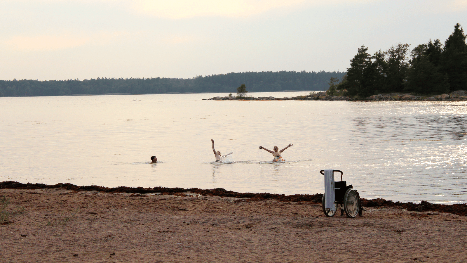 Barn som badar. Tom rullstol på stranden